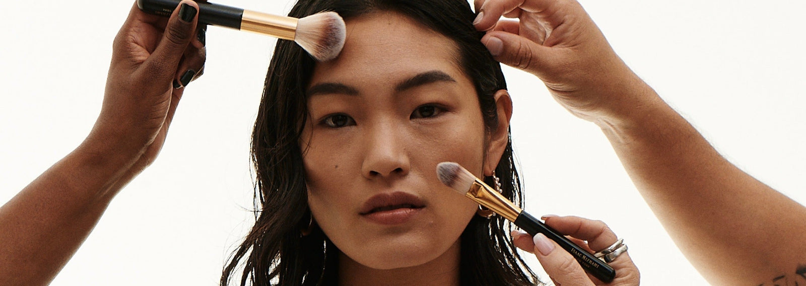 Three hands using makeup brushes on models face 